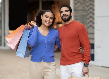 Photo for Sales Season. Happy Middle Eastern Spouses Shopping Together Posing With Paper Shopper Bags Standing In Modern Supermarket Outside. Shot Of Contented Buyers Embracing Outside. Discount Offer - Royalty Free Image