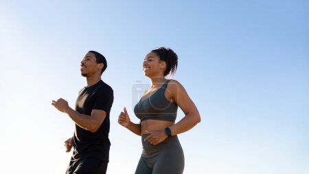 Téléchargez les photos : Glaad millénariste afro-américaine femme et homme en tenue de sport courir sur fond de ciel. Entraînement matinal, soins du corps et soins de santé, jogging ensemble, perte de poids et vitalité en plein air - en image libre de droit