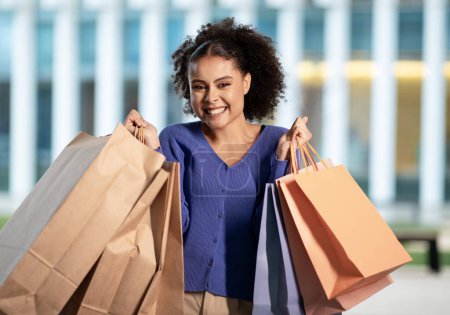 Photo for Great Shopping Offer. Excited African American Woman Posing With Many Shopper Paper Bags Smiling To Camera Standing Near Modern Mall Outside. Shot Of Happy Shopaholic Lady. Consumerism - Royalty Free Image