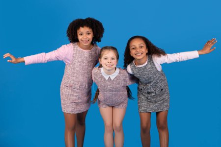 Photo for Smiling teen african american and european girls have fun, enjoy spare time together, dancing isolated on blue studio background. Childhood, friendship relationship, lifestyle and study - Royalty Free Image