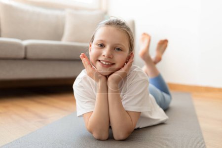Photo for Positive european teenager girl in sportswear lies on mat, enjoys workout in living room interior. New normal, training, body care sport, yoga and fitness at home, active lifestyle - Royalty Free Image