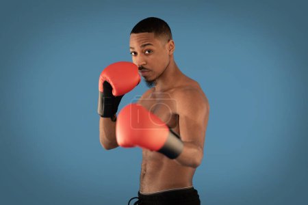 Photo for Athletic handsome shirtless young black guy wearing red gloves professional sportsman boxing over blue studio background, copy space. Combat sport, workout, cardio, sports lifestyle concept - Royalty Free Image