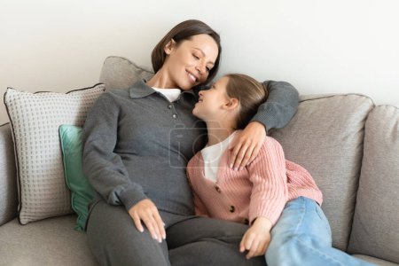 Photo for Smiling european millennial mother hugging little girl, have fun together, enjoy time in living room interior. Relax, break and rest at weekend, love, relationship at home - Royalty Free Image