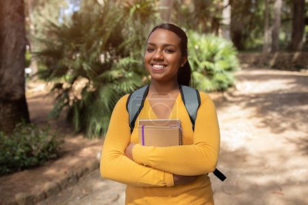 Photo for Happy brazilian female student standing outdoors with workbooks in hands, excited lady posing outside in park, carrying backpack and smiling at camera, free space - Royalty Free Image