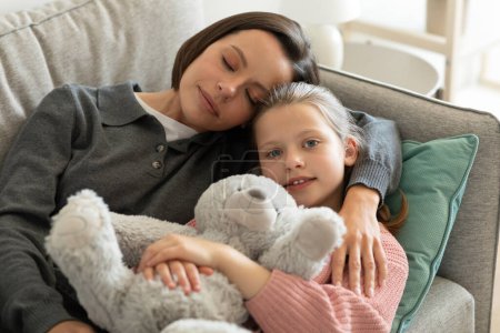 Photo for Happy tired european millennial mom hugging little girl with toy, sleeping on sofa in living room interior. Break, rest and relax at weekend, spare time, love and relationships at home - Royalty Free Image