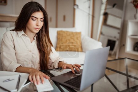Photo for Serious busy smart millennial european female manager typing on computer, check bill, finance, pay taxes in living room interior. Bookkeeping, freelance, work and business at home - Royalty Free Image