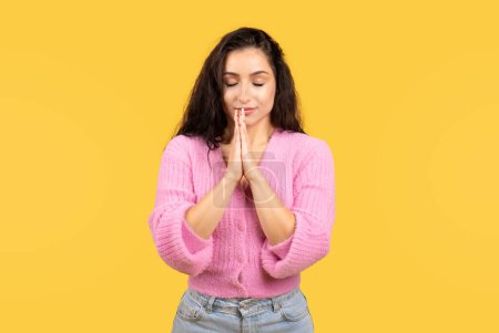 Photo for Serious pretty millennial middle eastern lady in casual with closed eyes prays, makes wish isolated on yellow background, studio. Dream, lifestyle, human emotions, ad and offer - Royalty Free Image