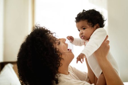 Photo for Cheerful young african american curly woman playing with little child, enjoy relax and tender moment together, have fun in bedroom interior. Baby care, love, relationship mother and child at home - Royalty Free Image