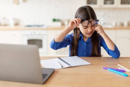 Photo for Eyestrain Problem. Tired Schoolgirl Rubbing Sore Eye Doing Homework On Laptop, Suffering From Fatigue And Dry Eyes Syndrome, Wearing Glasses Sitting At Desk At Home. Children Eyesight Issues - Royalty Free Image
