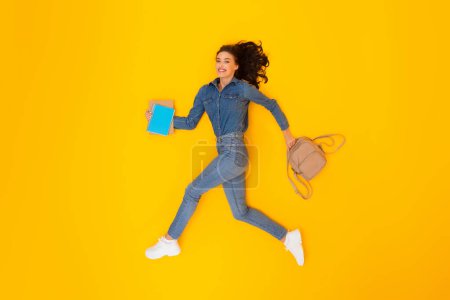 Photo for Cheerful Woman Running Holding Backpack And Copybooks Posing Smiling To Camera Over Yellow Background In Studio. Modern Education Concept. Full Length Shot Of Female Student - Royalty Free Image