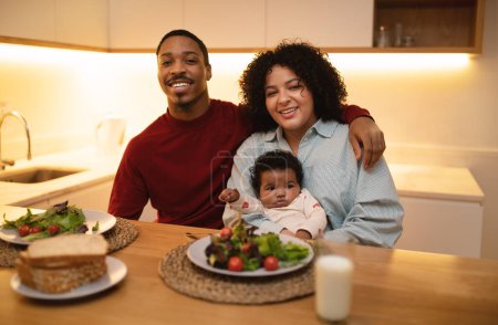 Photo for Happy multicultural family with their little baby daughter sitting at kitchen table, have dinner together, black man husband hugging hispanic woman wife. Concept of interracial family - Royalty Free Image