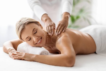 Photo for Beautiful middle aged woman receiving relaxing shoulder massage from professional therapist in spa salon, closeup shot of attractive mature female enjoying wellness treatment in beauty studio - Royalty Free Image