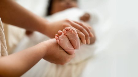 Photo for Young african american female hold cute legs of little child, lie on bed, rest in children room, cropped, blurred. Family, kid care, motherhood and love, mom and baby at home - Royalty Free Image