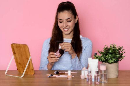 Photo for Happy cheerful attractive brunette young hispanic woman in casual outfit sitting at desk over pink studio background, doing manicure, checking brand new colorful nail polish, copy space - Royalty Free Image