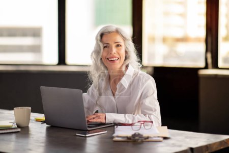 Photo for Happy Middle Aged Business Woman Using Laptop Working Online Smiling To Camera Posing At Workplace, Sitting At Desk In Modern Office. Female Manager Browsing Internet On Computer - Royalty Free Image