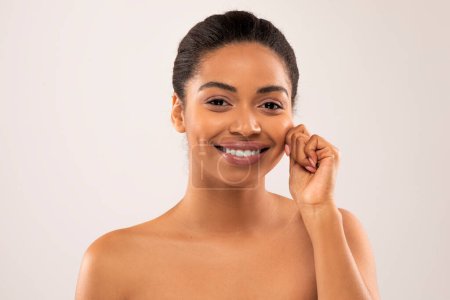 Photo for Cheerful happy smiling attractive naked millennial african american woman touching her cheek and smiling on studio background, showing young smooth glowing skin, closeup - Royalty Free Image