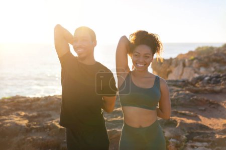 Photo for Body care, health care together. Glad millennial african american family in sportswear running, doing exercises for hands, stretching on ocean beach at sunrise. Morning workout, weight loss outdoor - Royalty Free Image