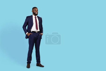 Photo for Smiling Young Black Businessman In Suit Looking At Copy Space While Standing Over Blue Studio Background, Handsome African American Male Entrepreneur Enjoying Business Offer, Full Length - Royalty Free Image