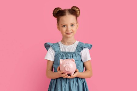 Photo for Economy Concept. Portrait Of Cute Little Girl Holding Piggy Bank In Hands And Smiling At Camera, Beautiful Preteen Female Child Enjoying Saving Money Or Advertising Wise Investments, Pink Background - Royalty Free Image