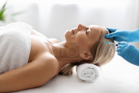 Photo for Side view of beautiful middle aged woman getting hair treatment at beauty salon, female patient having mesotherapy session at aesthetic clinic, therapist hands in gloves making injection in scalp - Royalty Free Image