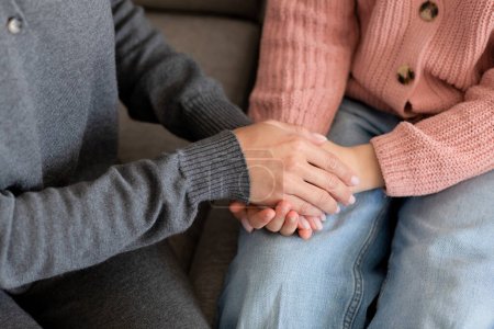 European millennial mother holding hands calms sad teenage girl in living room interior, cropped, top view, close up. Love, support, care, advice and relationships at home