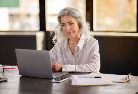Photo for Mature Business Lady Using Laptop Computer Working Online Sitting At Desk In Modern Office. Businesswoman Typing And Browsing Internet On PC At Workplace. Career And Technology - Royalty Free Image