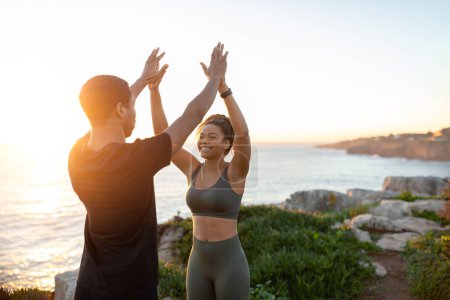 Photo for Happy young african american family athletes in sportswear give high five enjoy sport teamwork and good workout resulton at ocean beach, sun flare. Body care together in morning outdoor - Royalty Free Image