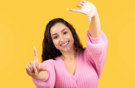 Photo for Cheerful millennial arab female in casual making lens gesture with hands isolated on yellow background, studio. Shooting video, sale, ad and offer, lifestyle, work and study, creating idea for blog - Royalty Free Image