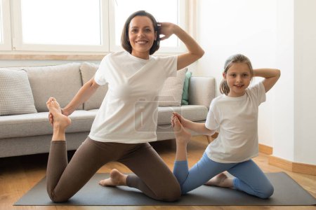 Téléchargez les photos : Positif actif européen millénariste maman et adolescente en vêtements de sport faire de l'exercice, profiter de l'entraînement, pratiquer le yoga dans le salon intérieur. Soins du corps ensemble, sport et fitness à la maison - en image libre de droit