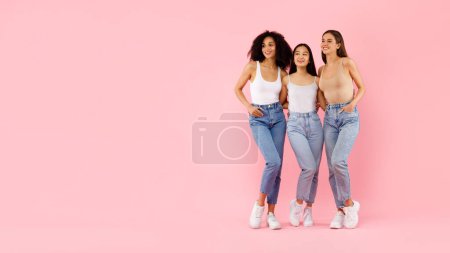 Téléchargez les photos : Portrait intégral de trois jeunes femmes multiethniques étreignant et posant, debout dans un studio isolé sur fond rose, panorama avec espace libre, bannière - en image libre de droit
