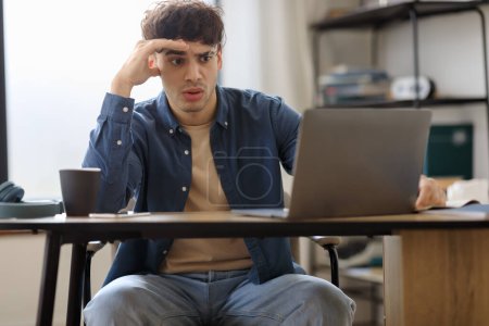 Téléchargez les photos : Oups. L'homme arabe stressé utilisant un ordinateur portable regardant l'écran et lisant de mauvaises nouvelles assis au bureau dans le bureau moderne. Guy travaillant en ligne et ayant des problèmes au travail. Concept des questions opérationnelles - en image libre de droit