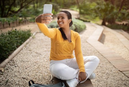 Foto de Emocionada dama brasileña tomando selfie en el teléfono inteligente al aire libre, estudiante tomando descanso y la captura de fotos con el teléfono móvil después de las clases, espacio de copia - Imagen libre de derechos
