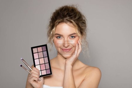Photo for Beautiful lady with eye shadow makeup palette and brushes posing over grey background and smiling at camera, banner. Woman with healthy perfect skin. Cosmetology, professional makeup products - Royalty Free Image