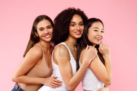 Photo for Happy three diverse ladies posing and hugging, standing on pink studio background and smiling at camera. Female friendship concept - Royalty Free Image