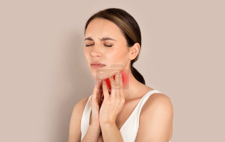 Unhappy young brunette woman with closed eyes wearing white top suffering from pain in throat, touching red inflamed zone on her neck, panorama with empty space, beige studio background