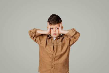 Photo for Frightened shocked little child 6 years old in shirt presses his hands to head isolated on gray studio background. Problems in school, childhood, fear, pupil emotions, ad and offer - Royalty Free Image