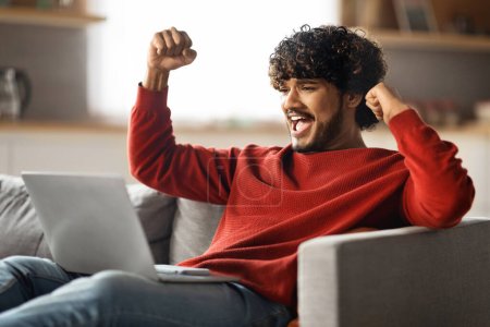 Great News. Portrait Of Happy Excited Indian Man Celebrating Success With Laptop At Home, Overjoyed Young Eastern Guy Looking At Computer Screen, Raising Fists And Exclaining With Joy, Closeup