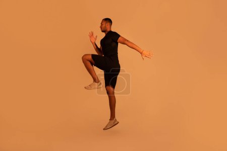 Photo for Determined Black Fitness Guy Exercising Doing Elbow To Knee Crunches Or Jumping Posing Over Beige Studio Background, Full Length Shot. Healthy Lifestyle, Sport And Workout Concept - Royalty Free Image