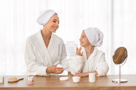 Photo for Cute Little Girl And Her Mom Applying Moisturising Cream While Sitting At Dressing Table At Home, Loving Young Mother And Preteen Female Child Having Domestic Spa Day, Enjoying Spending Time Together - Royalty Free Image