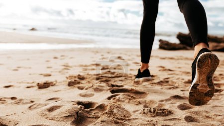 Foto de Vista trasera cercana de los pies femeninos, señora corriendo sobre arena, haciendo ejercicio matutino en la playa del océano, panorama con espacio de copia gratis, recortado - Imagen libre de derechos