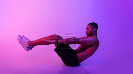 Téléchargez les photos : Homme Afro-Américain Sportif Faire V-Ups Abs Exercice Flexing Muscles abdominaux pendant l'entraînement sur fond violet. Fitness Guy faisant des craquements avec les jambes levées et les bras écartés. Panorama - en image libre de droit
