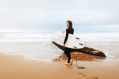 Téléchargez les photos : Vacances d'été et concept de sport extrême. Jeune femme marchant avec planche de surf sur la plage de l'océan, dame allant sur la session de surf sur l'emplacement tropical, pleine longueur, espace libre - en image libre de droit