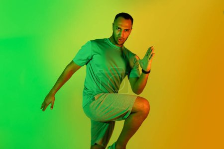 Téléchargez les photos : Résolu homme afro-américain s'exerçant à regarder la caméra faisant coude à genou Crunch debout sur fond vert néon en studio. Concept de motivation pour le sport et l'entraînement - en image libre de droit