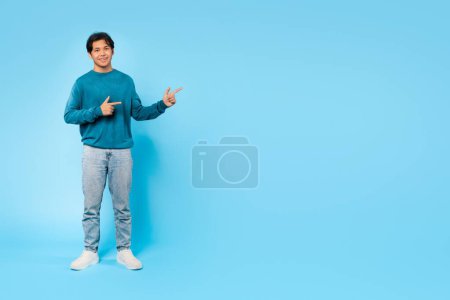 Téléchargez les photos : Regarde là. Japonais adolescent guy pointant doigt à côté de vide espace debout sourire à la caméra sur bleu studio fond. Garçon Publicité et recommander une offre montrant la direction. Prise de vue complète - en image libre de droit