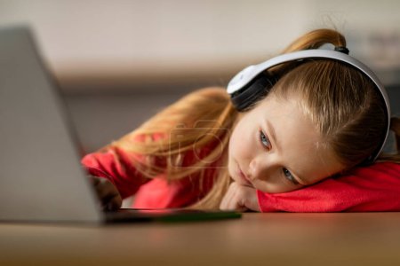 Photo for Burnout In Children. Upset Little Girl Leaning At Desk And Looking At Laptop Screen, Closeup Shot Of Bored Sad Preteen Female Child In Wireless Headphones Using Computer At Home, Suffering Apathy - Royalty Free Image