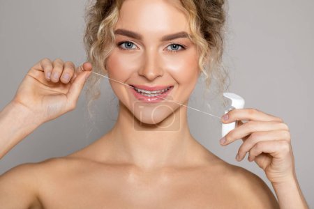 Photo for Portrait of happy young woman flossing mouth for clean oral hygiene, beautiful lady cleaning teeth with dental floss, isolated on grey studio background, closeup - Royalty Free Image