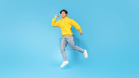 Téléchargez les photos : Positif asiatique adolescent garçon sautant posant et s'amusant publicité grande offre sur fond bleu studio. Étudiant posant en plein air souriant à la caméra. Panorama, pleine longueur - en image libre de droit