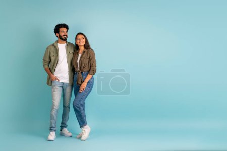 Photo for Amazing deal for two, time together. Loving cheerful beautiful young indian couple in casual embracing and looking at free space for advertisement on blue studio background, panorama - Royalty Free Image