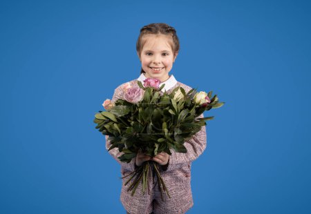 Téléchargez les photos : Souriant petite fille européenne avec bouquet de fleurs profiter anniversaire de printemps isolé sur fond bleu, studio. Salutation, fête, félicitations, enfance et émotions - en image libre de droit