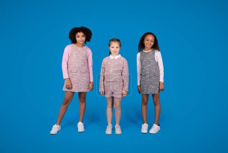 Photo for Smiling international little girlfriends pupils in casual isolated on blue background, studio, full length. Family friendship, study in school and education for children, childhood - Royalty Free Image